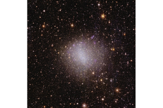 A glowing pink and white speck of light in the center of the image, surrounded by millions of specks of light representing distant cosmic objects.